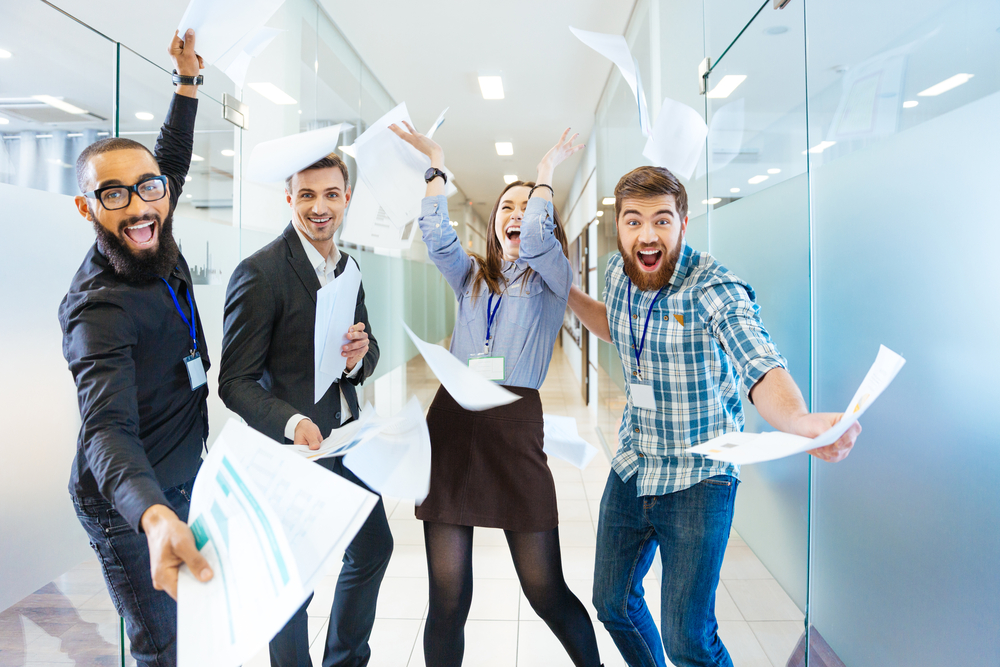 Group of joyful excited business people throwing papers and having fun in office